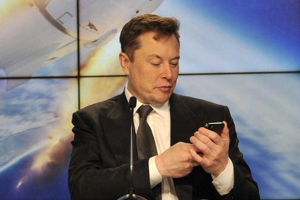 Elon Must checks out his phone amidst a press conference. (Source: Getty)