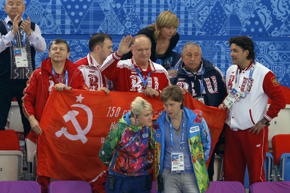 Russian Communist Party leader Gennady Zyuganov, center, waves and holds the Soviet Banner of Victory with lawmakers Yuri Afonin, second left, Nikolai Kharitonov, second right, both members of the Communist faction in the Russian parliament, as the venue protocol manager, bottom left, and the deputy venue manager partially block the banner during a flower ceremony for the short track speedskating competition at the Iceberg Skating Palace in Sochi, Russia, during the 2014 Winter Olympics on Friday, Feb. 21, 2014. Venue manager Svetlana Bazhanova, top, speaks with Communist Party spokesman Alexander Yushchenko, right. The banner is a replica of the flag raised by Soviet soldiers in Berlin in 1945, in victory over Nazi Germany. The International Olympic Committee forbids the display of political banners at Olympic venues. (AP Photo/Vadim Ghirda)