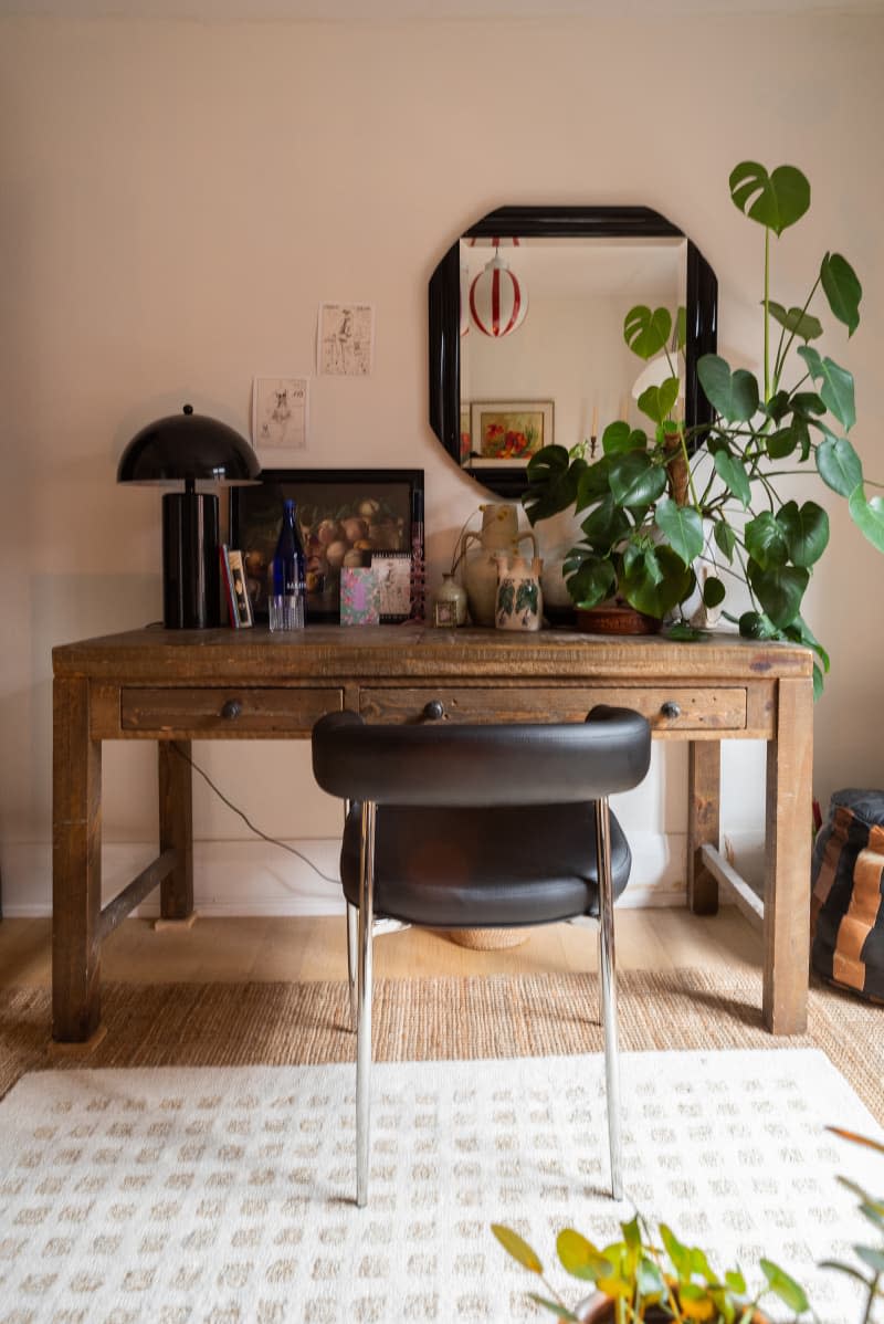 Wooden desk with black leather chair with large plant atop.