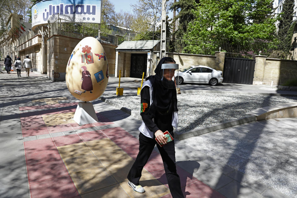 A woman wearing a face shield to protect against the new coronavirus walks on a sidewalk in northern Tehran, Iran, Saturday, April 4, 2020. In the first working day after Iranian New Year holidays authorities have allowed some government offices and businesses to re-open with limited working hours, when schools, universities, and many businesses still are ordered to be closed aimed to prevent the spread of the virus. (AP Photo/Vahid Salemi)