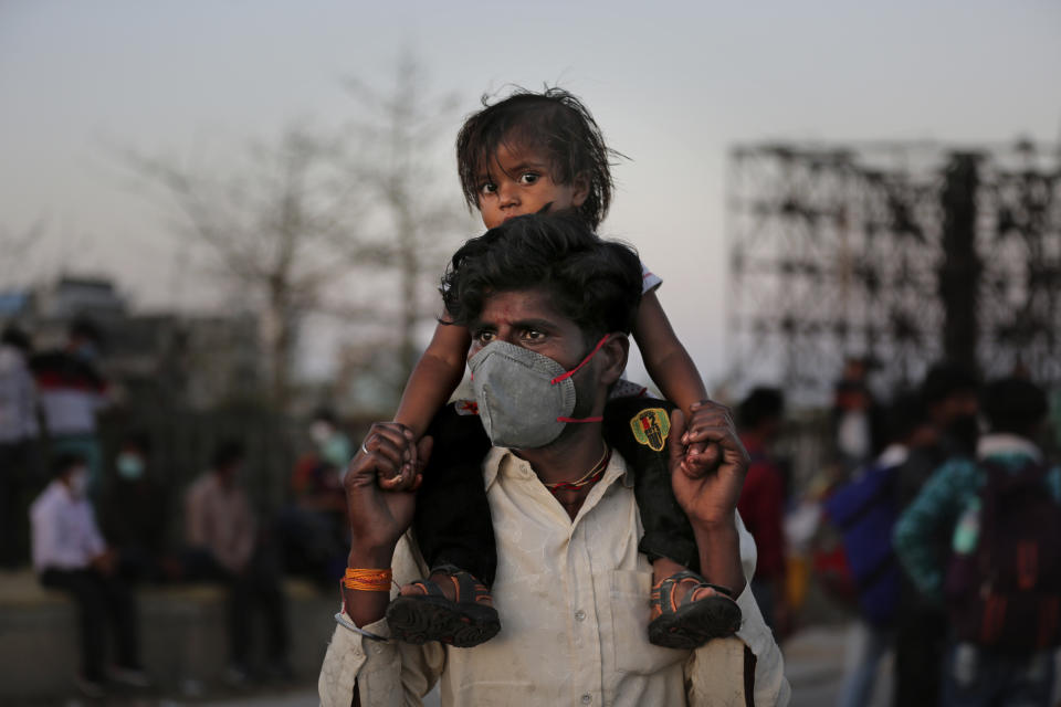 An Indian migrant worker carries a child on his shoulders as they wait for transportation to their village following a lockdown amid concern over spread of coronavirus in New Delhi, India, Saturday, March 28, 2020. Authorities sent a fleet of buses to the outskirts of India's capital on Saturday to meet an exodus of migrant workers desperately trying to reach their home villages during the world's largest coronavirus lockdown. Thousands of people, mostly young male day laborers but also families, fled their New Delhi homes after Prime Minister Narendra Modi announced a 21-day lockdown that began on Wednesday and effectively put millions of Indians who live off daily earnings out of work. (AP Photo/Altaf Qadri)