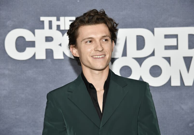 Tom Holland smiles in a green suit against a gray background.