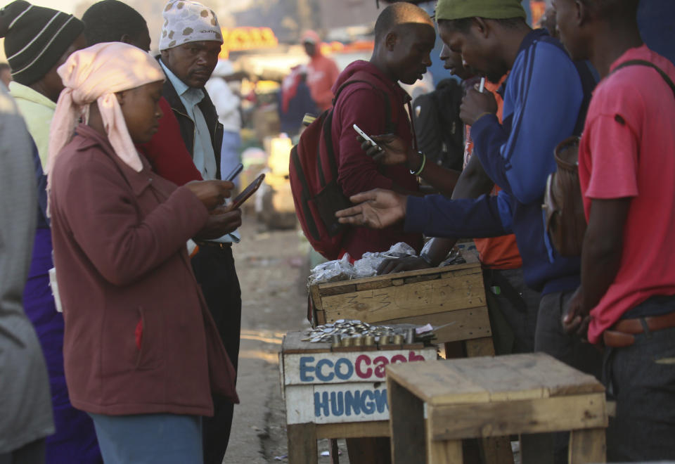 In this photo taken Thursday, Aug. 8, 2019, vendors are seen on their mobile phones while selling cash at a premium in Harare, Zimbabwe. With inflation soaring and cash in short supply, many Zimbabweans transfer funds using their mobile phones and pay a premium to get currency. (AP Photo/Tsvangirayi Mukwazhi)