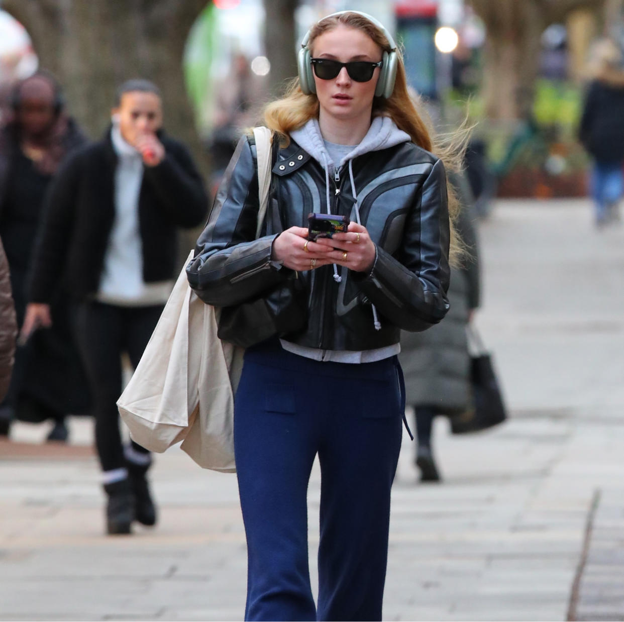  Sophie Turner in a leather jacket, blue pants, and a hoodie. 