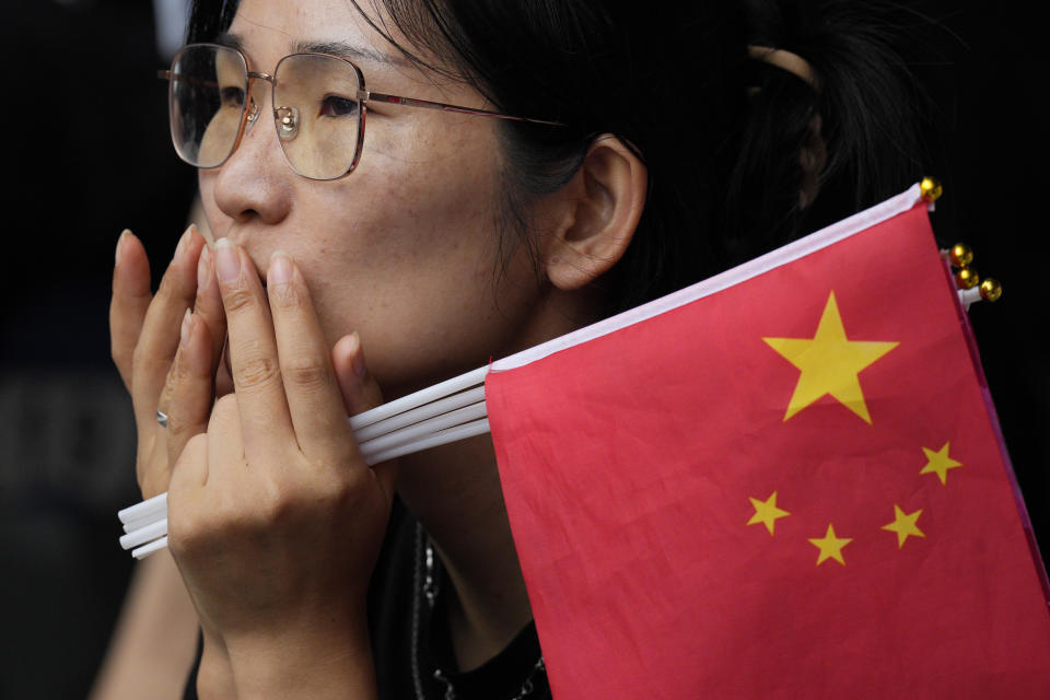 A woman holds Chinese flags as she watches the athletics competition at the 19th Asian Games in Hangzhou, China, Saturday, Sept. 30, 2023. (AP Photo/Vincent Thian )
