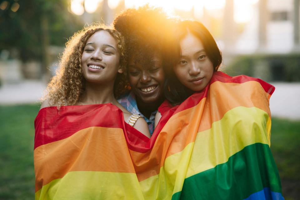 Three people wrapped in a pride flag.