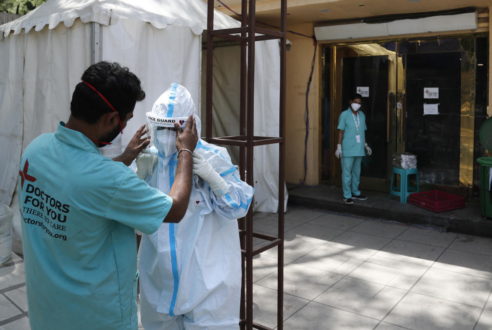 FILE- In this April 19, 2021, file photo, a health worker adjusts the face shield of another as she prepares to go inside a quarantine center for COVID-19 patients in New Delhi, India. As India suffers a bigger, more infectious second wave with a caseload of more than 300,000 new cases a day, the country’s healthcare workers are bearing the brunt of the disaster. (AP Photo/Manish Swarup, File)