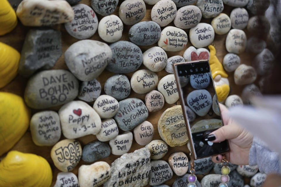 At the request of families, Rima Samman photographs particular names of people who died from coronavirus at the Rami's Heart COVID-19 Memorial in Wall Township, N.J., Wednesday, Oct. 27, 2021. The memorial, which started out on a jersey shore beach made of shells and rocks, has found a permanent home at Allaire Community Farm. Started by Samman and named after her brother Rami, who was died from coronavirus, it has grown to more than 4,000 victims' names, with dozens of new names added every week. (AP Photo/Seth Wenig)