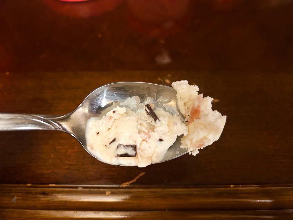 A metal spoon with white ice cream with pink and chocolate chunks in it