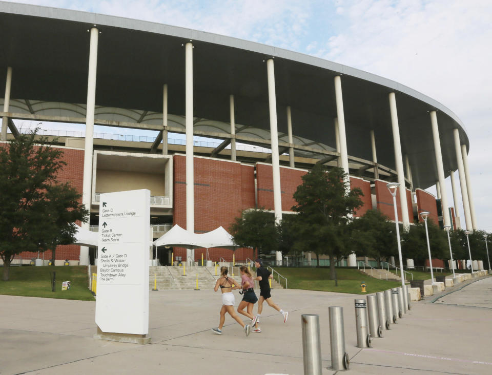 Baylor students jog past Baylor University's McLane Stadium, Thursday, Sept. 17, 2020, in Waco, Texas. Baylor’s season opener against Houston, scheduled less than a week ago, was one of two FBS NCAA college football games postponed Friday, Sept. 18, 2020, the day before before they were supposed play. (Rod Aydelotte/Waco Tribune-Herald via AP)