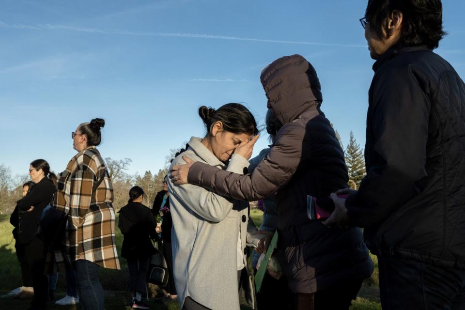 A woman rests her face in her palm while being comforted by another person.