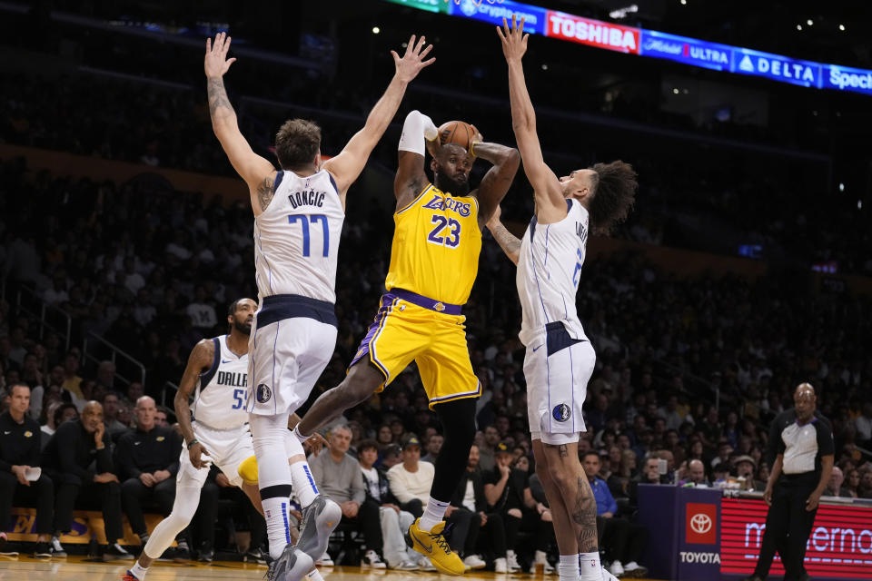 Los Angeles Lakers forward LeBron James (23) passes the ball from between Dallas Mavericks guard Luka Doncic (77) and center Dereck Lively II (2) during the first half of an NBA basketball game Wednesday, Nov. 22, 2023, in Los Angeles. (AP Photo/Marcio Jose Sanchez)