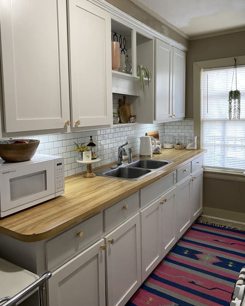 kitchen with pale gray cabinets, white subway tile backsplash, and black and white patterned wallpaper after makeover