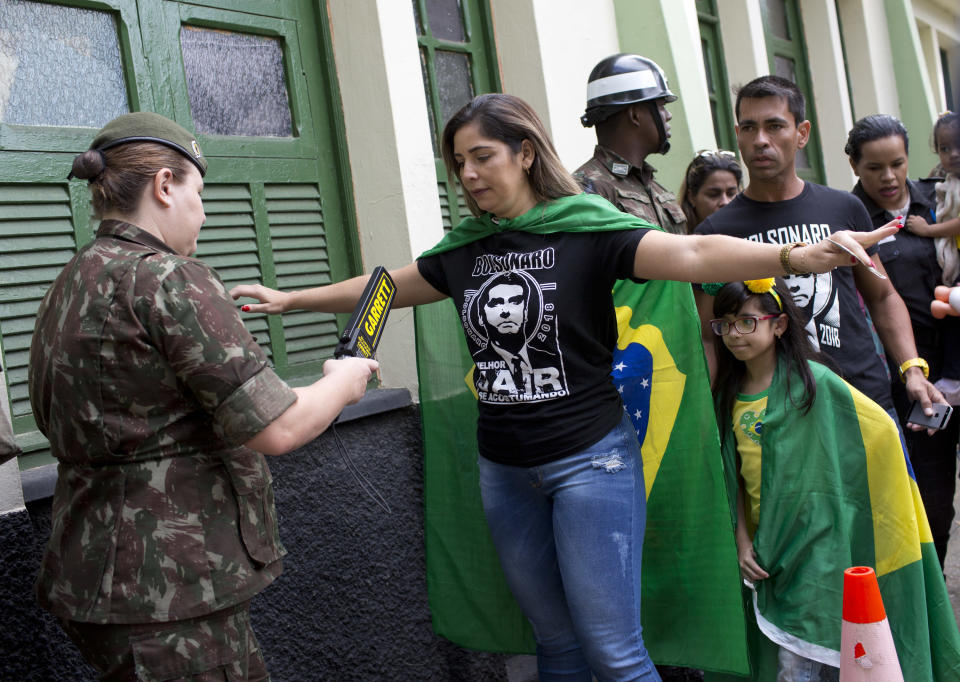 A supporter wearing a T-shirt of Jair Bolsonaro, presidential candidate with the Social Liberal Party, is checked by an army police at a polling station in Rio de Janeiro, Brazil, Sunday, Oct. 28, 2018. (AP Photo/Silvia Izquierdo)