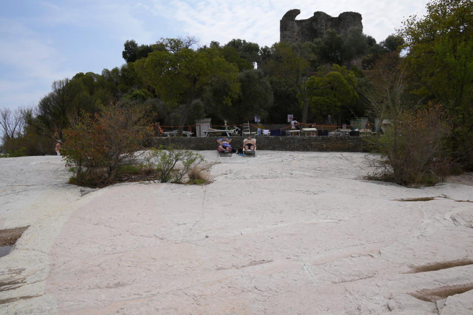 People sunbath on the peninsula of Sirmione, on Garda lake, Italy, Friday, Aug. 12, 2022. Lake Garda water level has dropped critically following severe drought resulting in rocks to emerge around the Sirmione Peninsula. (AP Photo/Antonio Calanni)