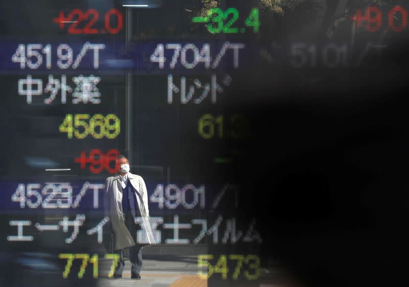 A man wearing a protective face mask is reflected on a stock quotation board outside a brokerage, amid the coronavirus disease (COVID-19) outbreak, in Tokyo