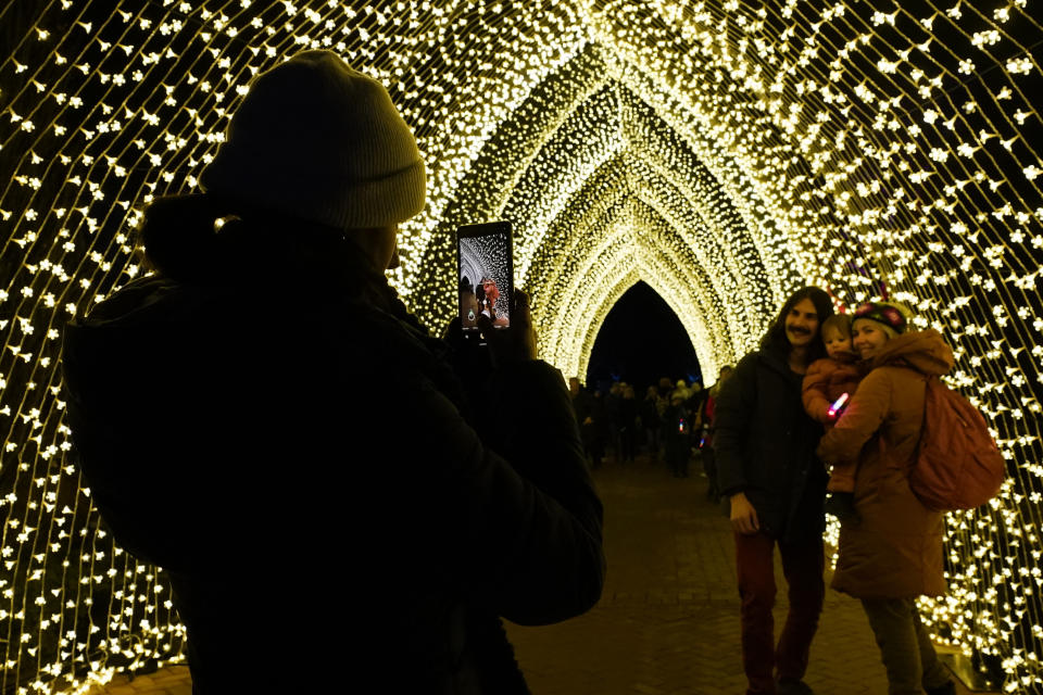Visitors finish the 1.3-mile Lightscape experience of light and music as they have a family portrait taken inside the 110-foot, 100,000 lights of "Winter Cathedral," created by Mandylights, at the Chicago Botanic Garden in Glencoe, Ill., on Thursday, Dec. 14, 2023. (AP Photo/Charles Rex Arbogast)