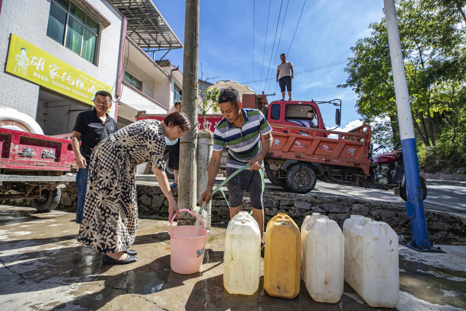 In this photo released by Xinhua News Agency, a worker stands on top of a truck distributing water to residents with a banner which reads "Luoping Drought Relief water truck" in Luoping village of Wushan County in southwestern China's Chongqing, Saturday, Aug. 13, 2022. Unusually high temperatures and a prolonged drought are affecting large swaths of China, affecting crop yields and drinking water supplies for thousands of people. (Huang Wei/Xinhua via AP)