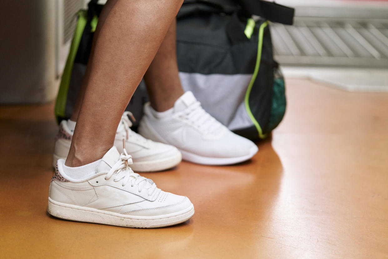 close-up of the legs of a girl seated inside a train with her backpack on the floor, side view white sneakers school shoes