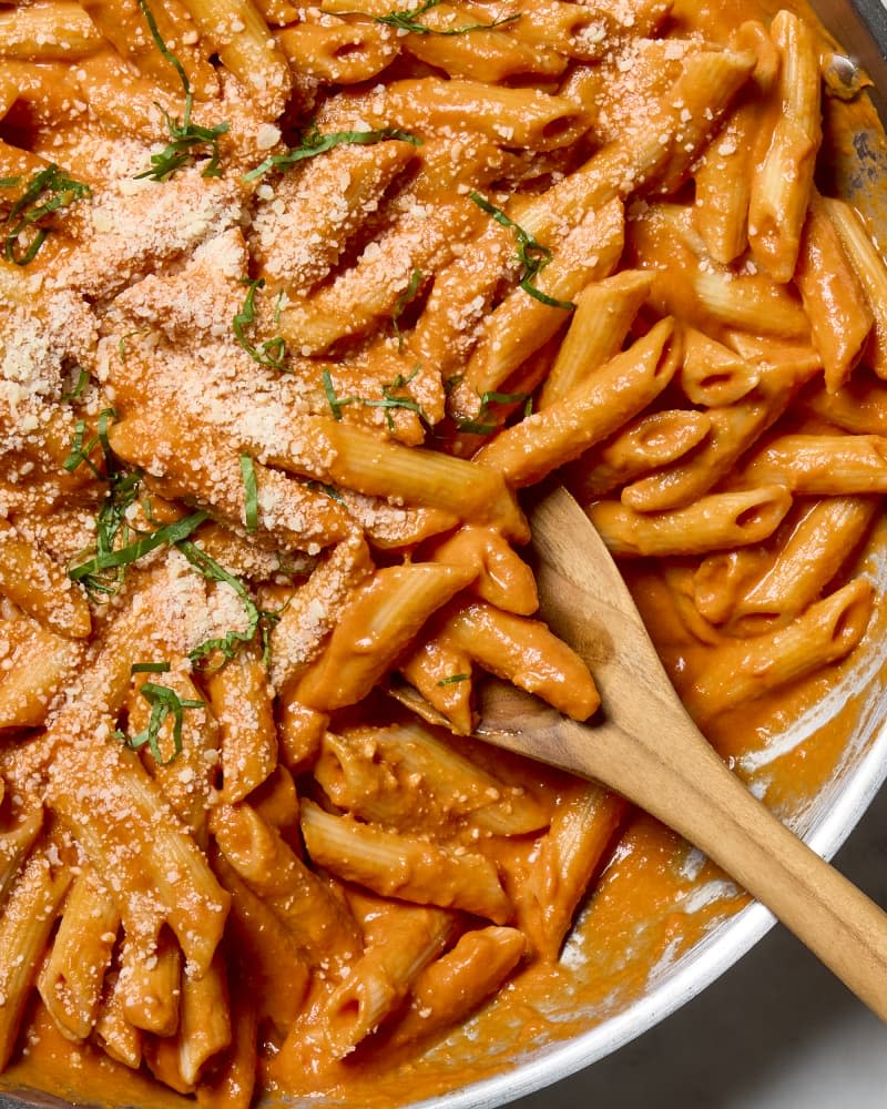 overhead shot of penne alla vodka in a pan with a wooden spoon resting inside.