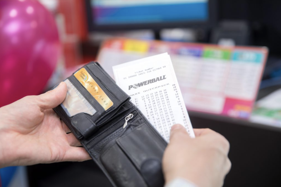 Picture of a wallet with someone taking out a Powerball lotto ticket in a news agents.