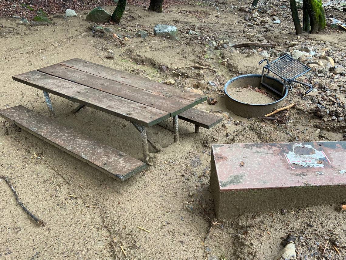 A picnic bench, bear box and fire ring are nearly buried in mud following a January 2023 flood that overwhelmed the South Fork Campground in California’s Sequoia National Park.