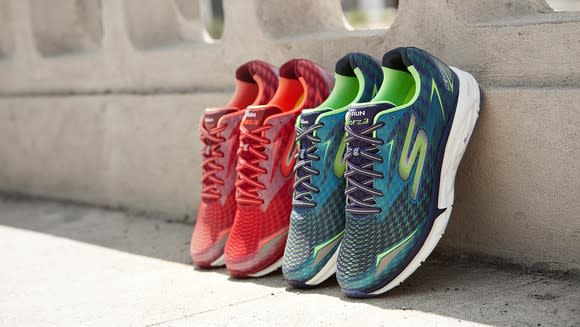 Two pairs of Skechers Go Run sneakers (one green and one red) propped up on a wall in the sun.