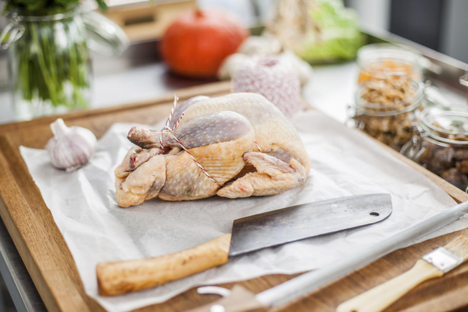 A photo of a raw whole chicken on a chopping board about to be roasted.