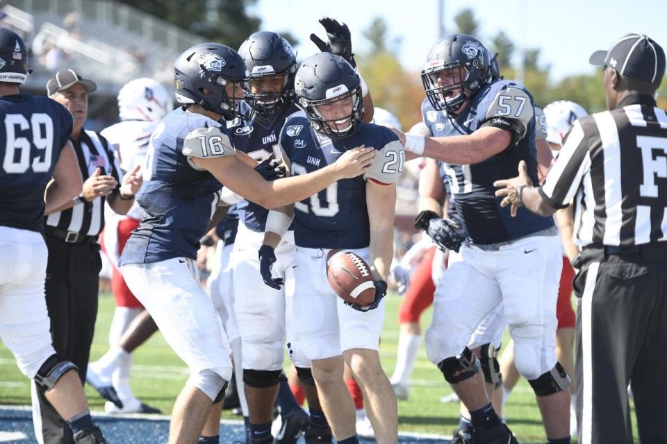 UNH quarterback Max Brosmer (16) and offensive lineman Patrick Flynn (57) celebrate with Dylan Laube after a touchdown.