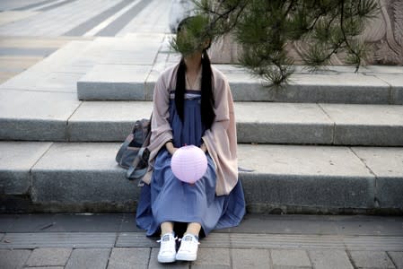 A girl dressed in "Hanfu" sits on a step as she waits to attend an event marking the traditional Qixi festival, at a park in Beijing, China