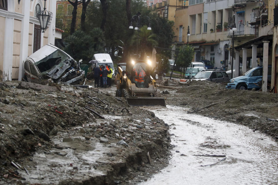 A caterpillar removes mud from a flooded road after heavy rainfall triggered landslides that collapsed buildings and left as many as 12 people missing, in Casamicciola, on the southern Italian island of Ischia, Saturday, Nov. 26, 2022. Firefighters are working on rescue efforts as reinforcements are being sent from nearby Naples, but are encountering difficulties in reaching the island either by motorboat or helicopter due to the weather. (AP Photo/Salvatore Laporta)