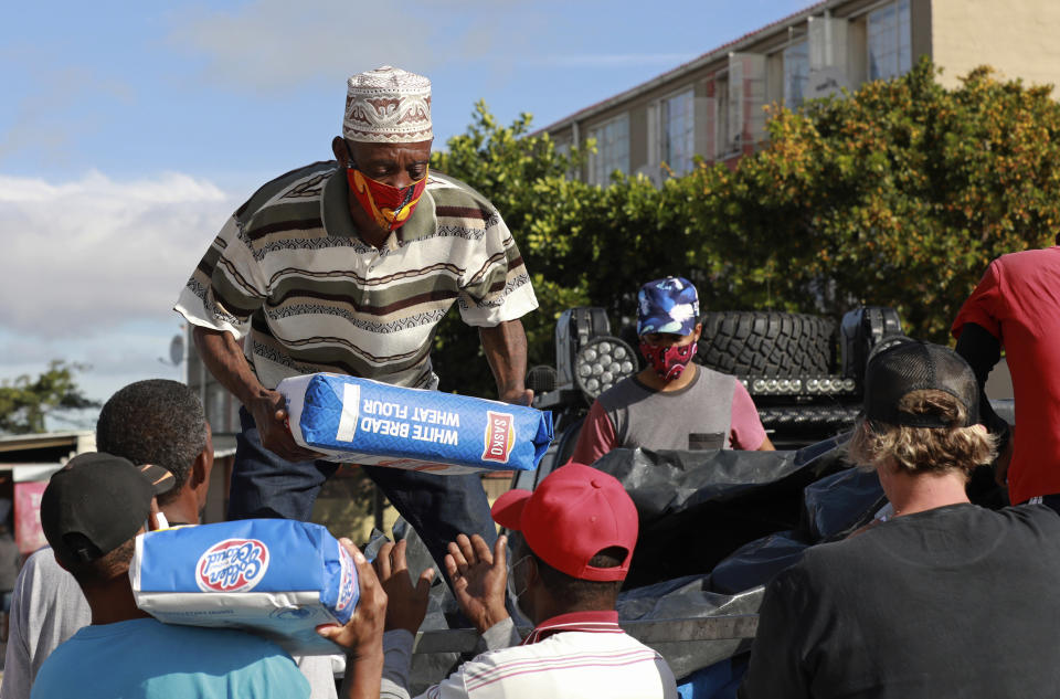 In this May 2, 2020, photo, Danny, a senior member of the Hard Livings gang, helps distribute food with rival gang members in Manenberg neighborhood in Cape Town, South Africa. The gangs are working together, under the direction of a preacher, to deliver bread, flour and vegetables to poor families who are struggling during South Africa's coronavirus lockdown. (AP Photo/Nardus Engelbrecht)