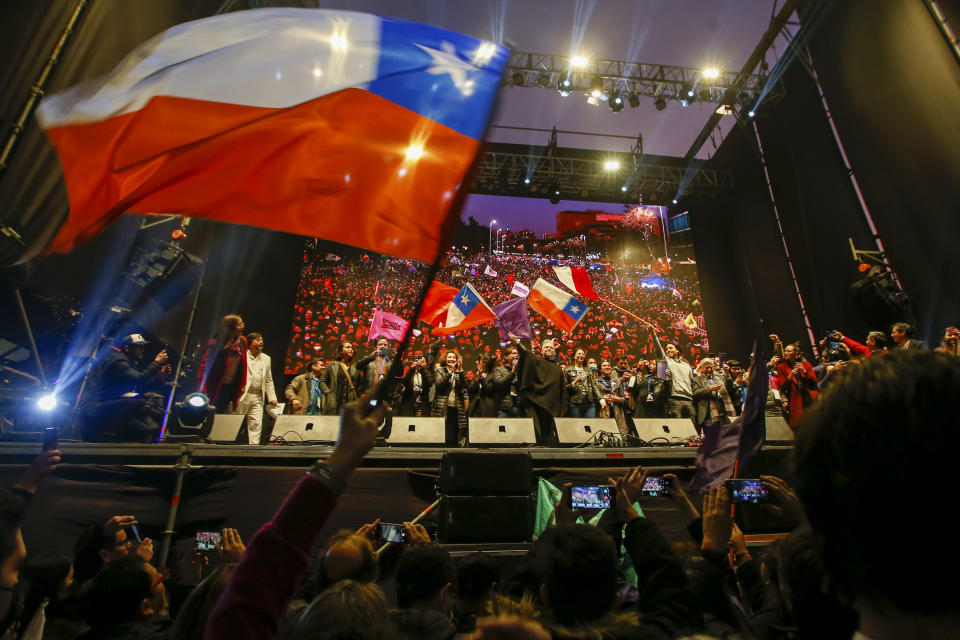 Constituent assembly delegates hold Chilean flags on a stage as demonstrators rally in favor of the proposed new Constitution in Santiago, Chile, Thursday, Sept. 1, 2022. Chileans have until the Sept. 4 plebiscite to study the new draft and decide if it will replace the current Magna Carta imposed by a military dictatorship 41 years ago. (AP Photo/Luis Hidalgo)