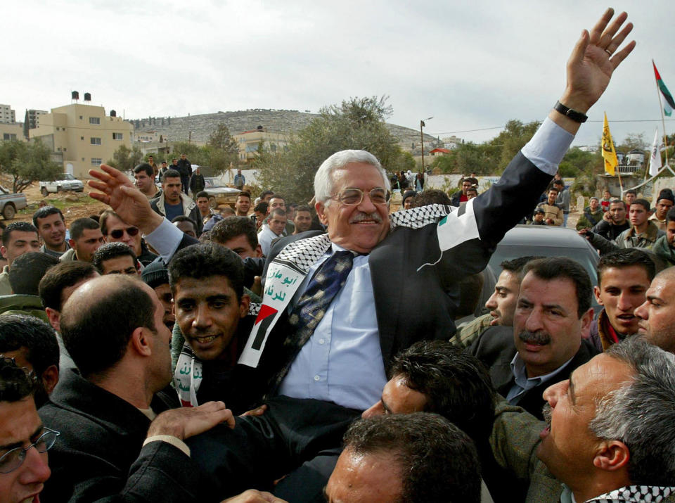 FILE - In this Dec. 30, 2004 file photo, then Interim Palestinian leader Mahmoud Abbas, and front-runner in the upcoming presidential elections, is carried by the Al Aqsa Martyrs' Brigades leader in West Bank, Zakaria Zubeidi, center left, during a campaign visit to the Jenin refugee camp. For nearly two decades, Zubeidi has been an object of fascination for Israelis and Palestinians alike, who have seen his progression from a child actor to a swaggering militant, to the scarred face of a West Bank theater promoting “cultural resistance” to Israeli occupation. In his latest act, he has emerged as one of Israel's most wanted fugitives after tunneling out of a high-security prison on Monday, Sept. 6, 2021 with five other Palestinian militants. (AP Photo/Enric Marti, File)