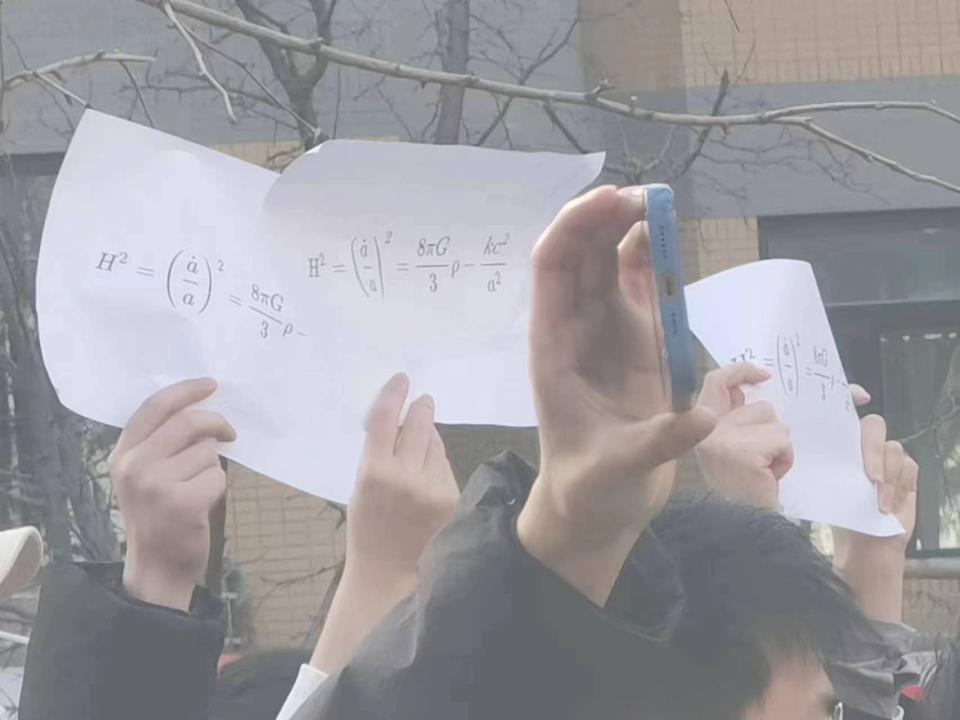 中國各地燒起「白紙抗議」，北京清華大學生舉起的白紙上，印了一組神祕的方程式。（翻攝自羅冠聰推特）