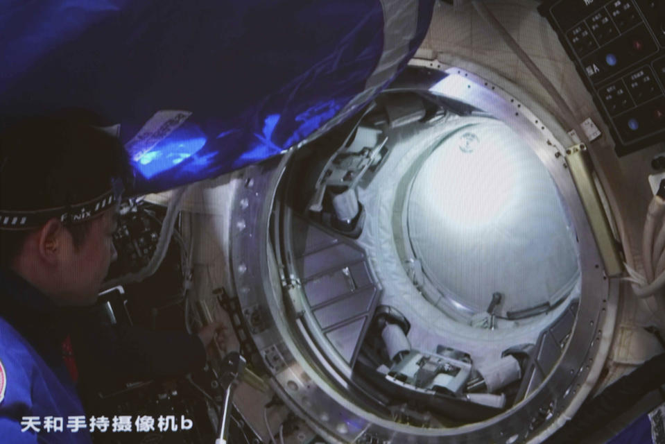 In this photo released by Xinhua News Agency, an image taken off the screen at the Beijing Aerospace Control Center shows Chinese astronaut Chen Dong opening the hatch door of the Wentian lab module on Monday, July 25, 2022. China added the laboratory to its permanent orbiting space station Monday as it moves toward completing the structure in coming months. Chinese characters on screen reads "Handheld camera b." (Guo Zhongzheng/Xinhua via AP)