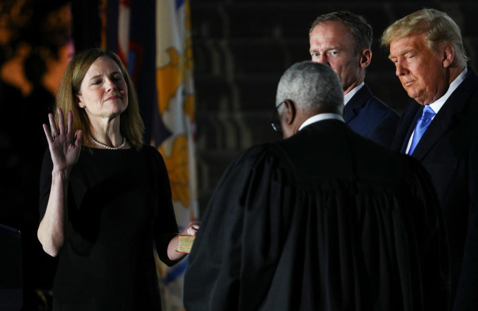 Judge Amy Coney Barrett is sworn in as an associate justice of the U.S. Supreme Court by Supreme Court Justice Clarence Thomas as her husband Jesse Barrett and President Donald Trump watch on the South Lawn of the White House in Washington, U.S., October 26, 2020.   REUTERS/Tom Brenner