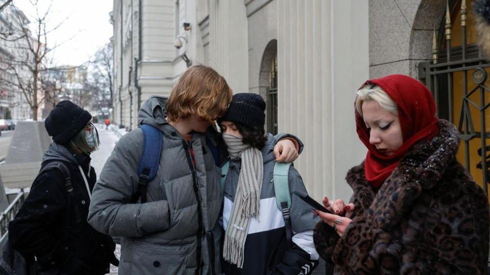 Ada with her arm around another young man, some other people near the Moscow High Court