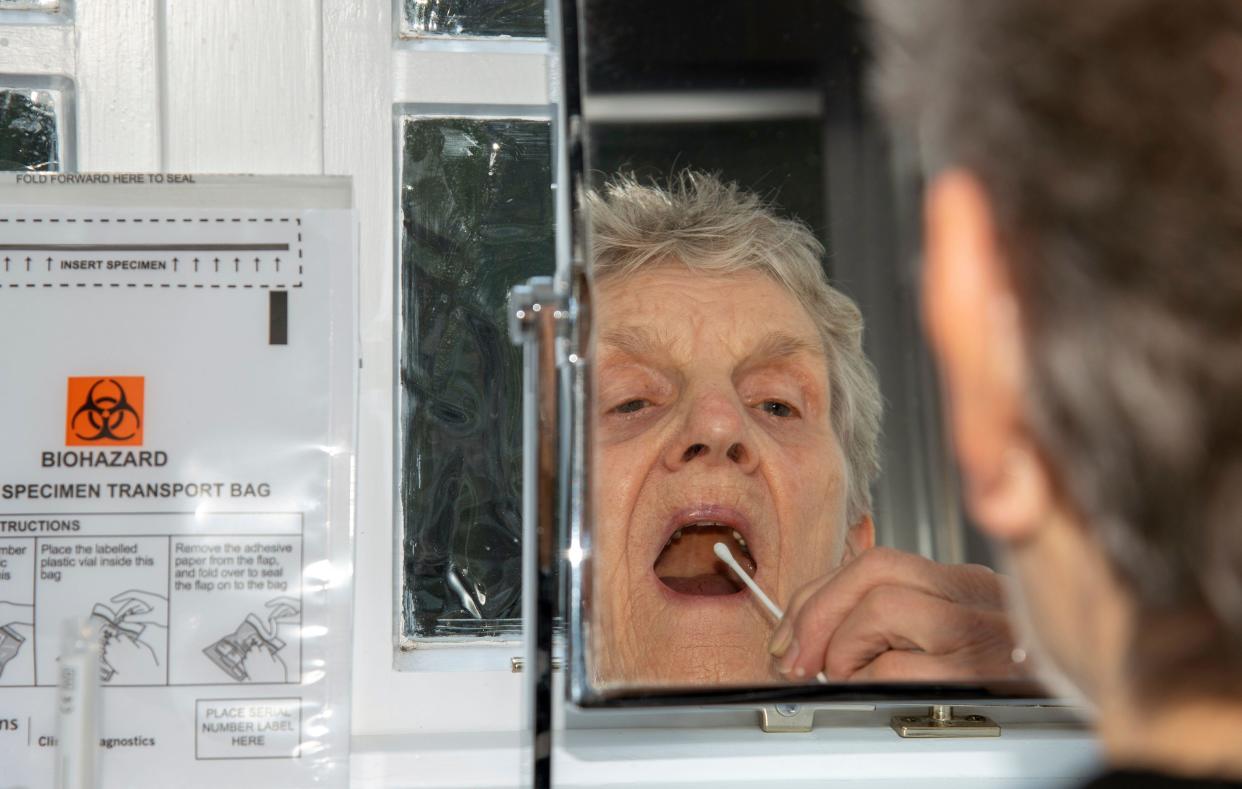 England, UK. 2021. Elderly woman using a swab from the Coronavirus Home Test Kit  about to take the nasel and throat swab test whilst looking in a mi