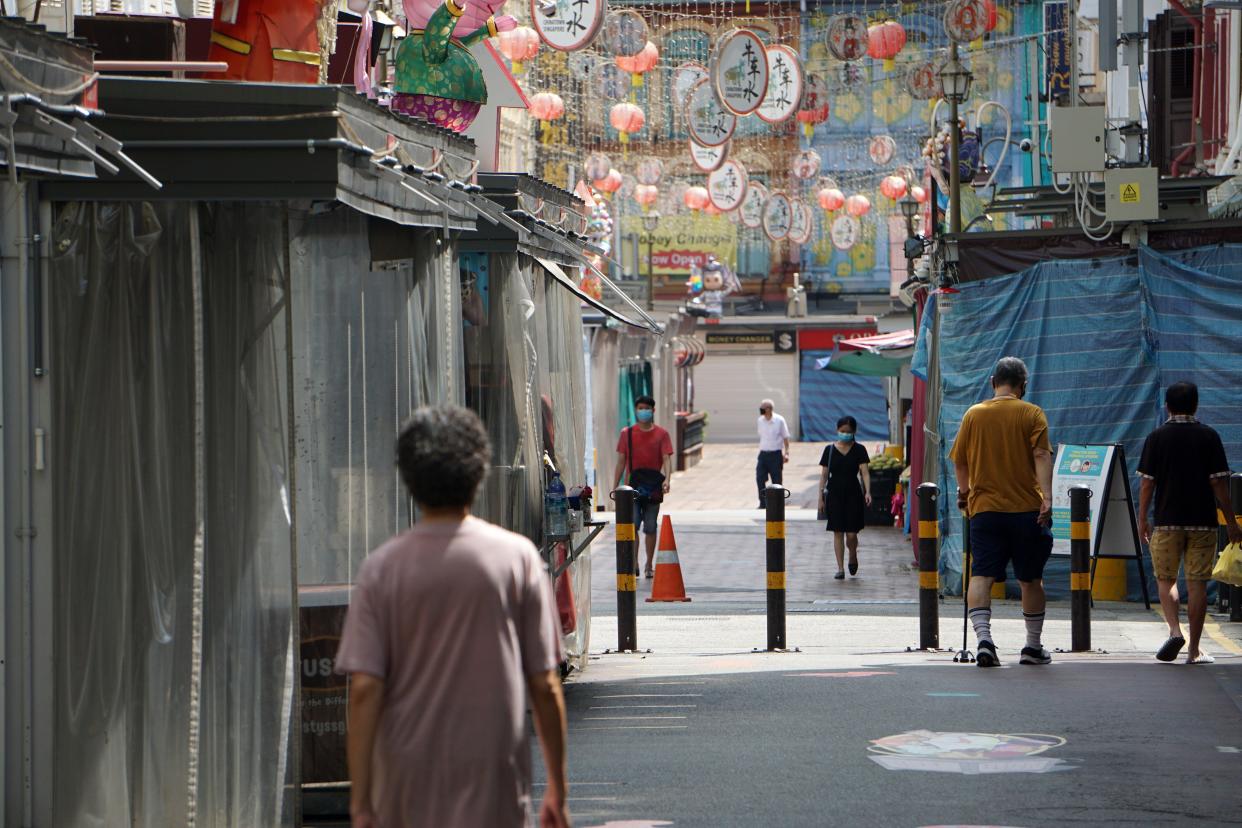 People wearing facemasks walk past closed shops in Chinatown on 13 April, 2020. (PHOTO: AFP via Getty Images)