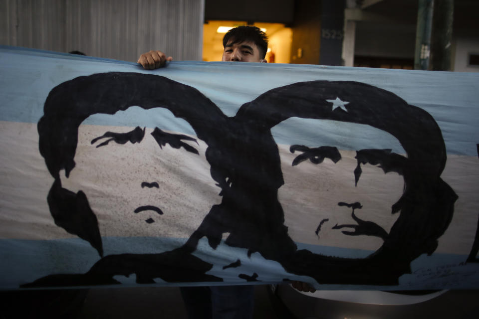 A soccer fan stands behind a banner featuring former soccer star Diego Maradona and Marxist revolutionary Ernesto "Che" Guevara, outside the Clinica Olivos, where Maradona will undergo surgery, in Buenos Aires, Argentina, Tuesday, Nov. 3, 2020. His personal doctor Leopoldo Luque, who is a neurologist, said Maradona has suffered a subdural hematoma, likely caused by an accident. The 1986 World Cup champion was admitted to a private hospital in la Plata with signs of depression on Monday, three days after his 60th birthday. (AP Photo/Natacha Pisarenko)
