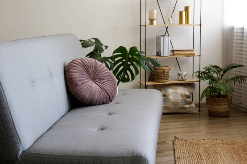 Minimalistic image, beige textile sofa with round cushions and floor shelf on blank wall background with lots of copy space for text. Empty room interior with only one sofa.pintuck round pillow on sofa