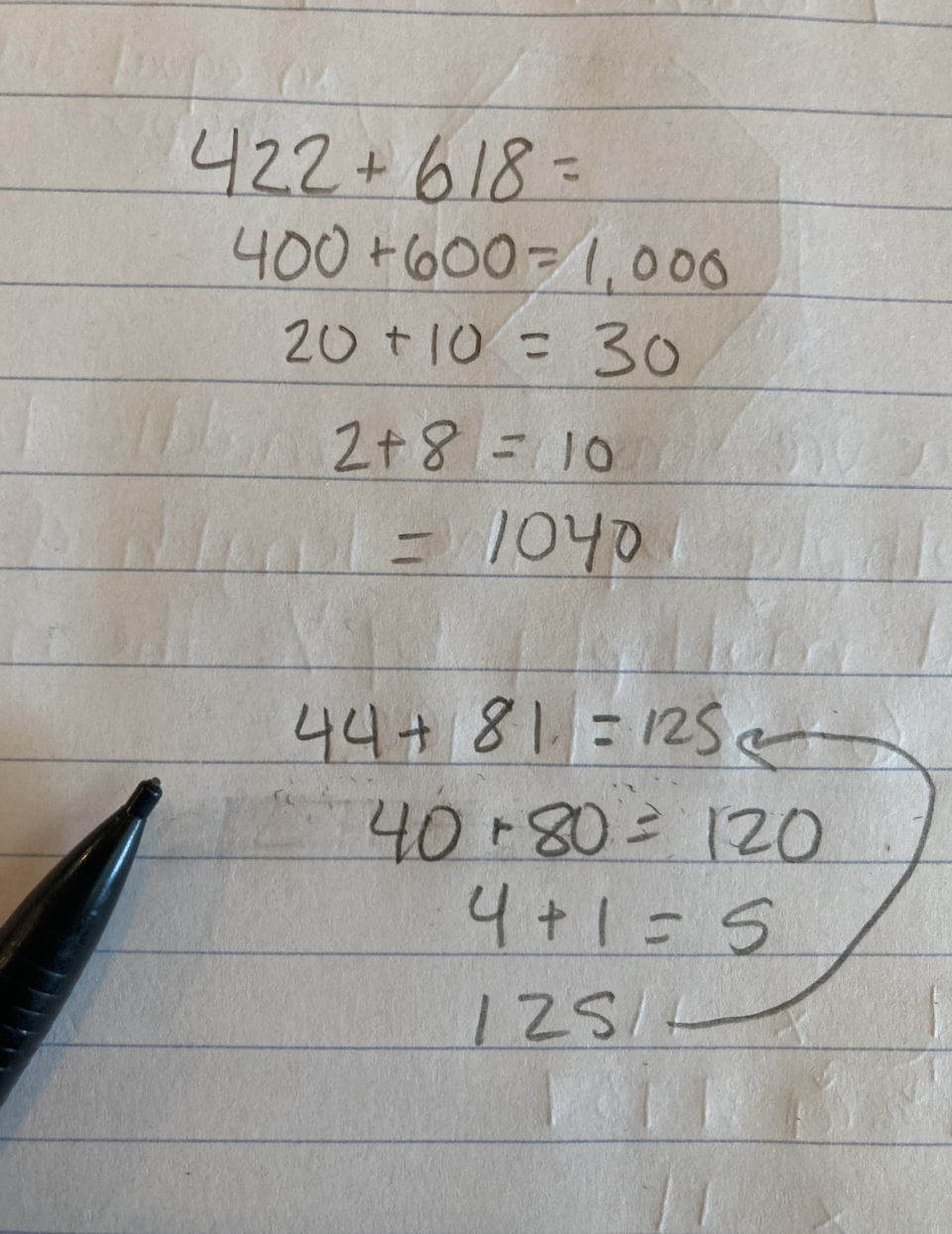 Handwritten math calculations on lined paper with a pen resting on it