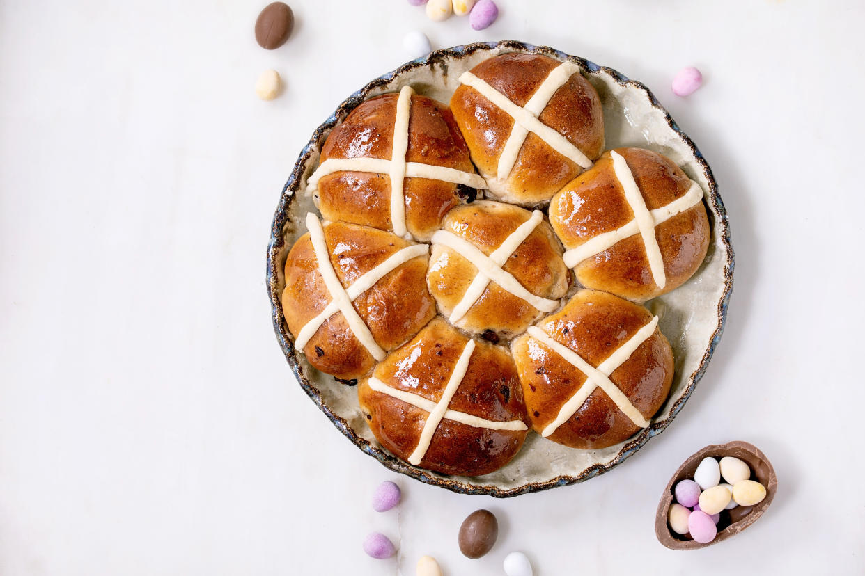 Homemade Easter traditional hot cross buns in ceramic dish with blossom flowers and chocolate candy eggs on white marble table. Flat lay, space. Easter holiday baking and treats. (Photo by: Natasha Breen/REDA&CO/Universal Images Group via Getty Images)