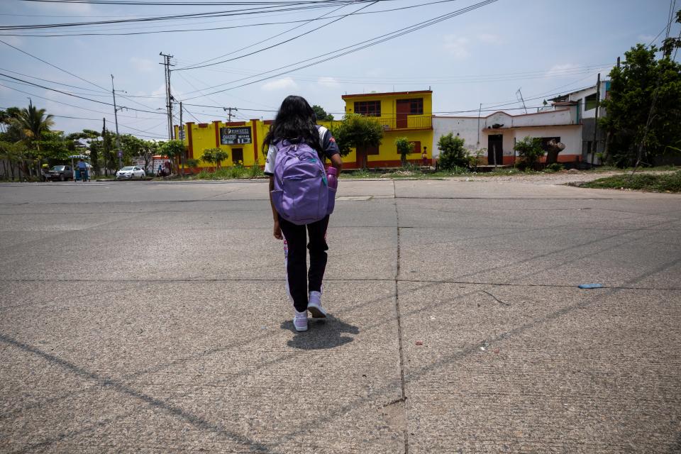 A girl wearing a purple backpack is seen from behind.