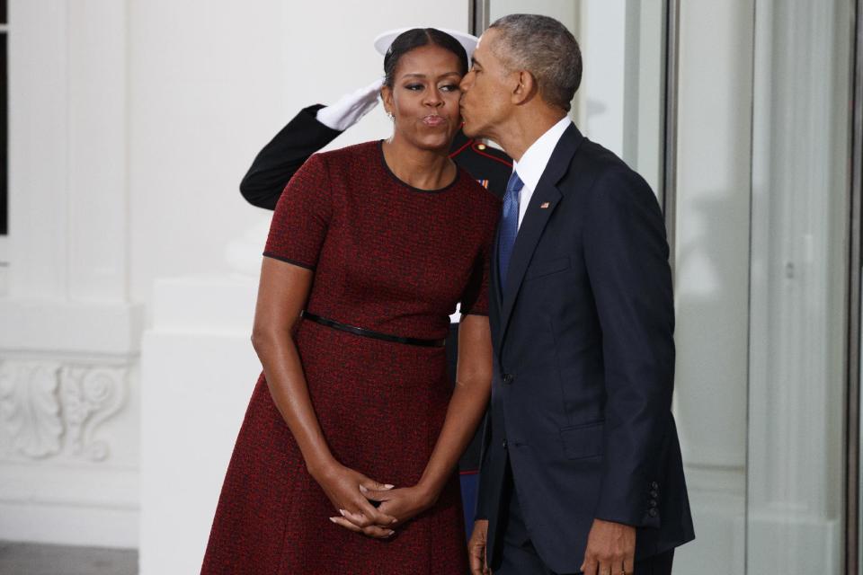 Michelle Obama (con su vestido rojo y negro) recibe un beso de su esposo, el expresidente Barack Obama.