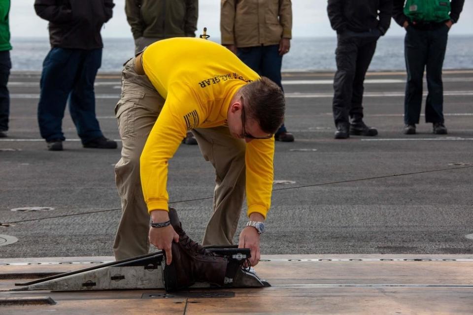 Lt. Cmdr. Alex Cleaveland secures a pair of boots to a catapult to be launched off a carrier flight deck