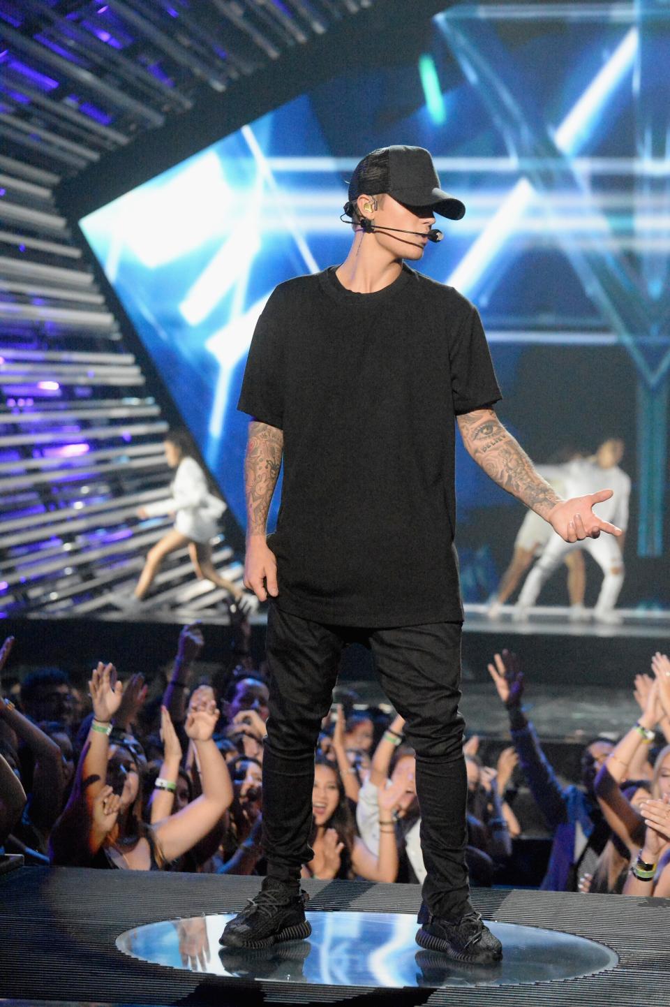 Justin Bieber performs on stage, wearing a dark t-shirt and pants, with fans reaching towards him