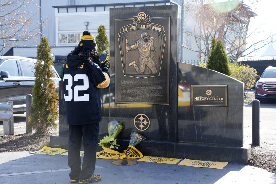 FILE - A fan takes a photo of the flowers and Terrible Towels placed at the Immaculate Reception memorial outside Acrisure Stadium on the Northside of Pittsburgh in memory of Pittsburgh Steelers Pro Football Hall of Fame running back Franco Harris, Wednesday, Dec. 21, 2022. While its Super Bowl commercial appearances are few, religion – Christianity especially – is entrenched in football culture. (AP Photo/Gene J. Puskar, File)