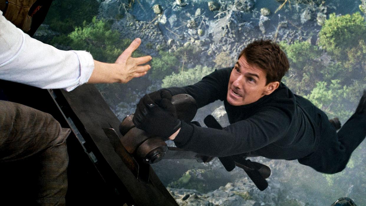  Ethan Hunt (Tom Cruise) hangs from a helicopter above a valley . 